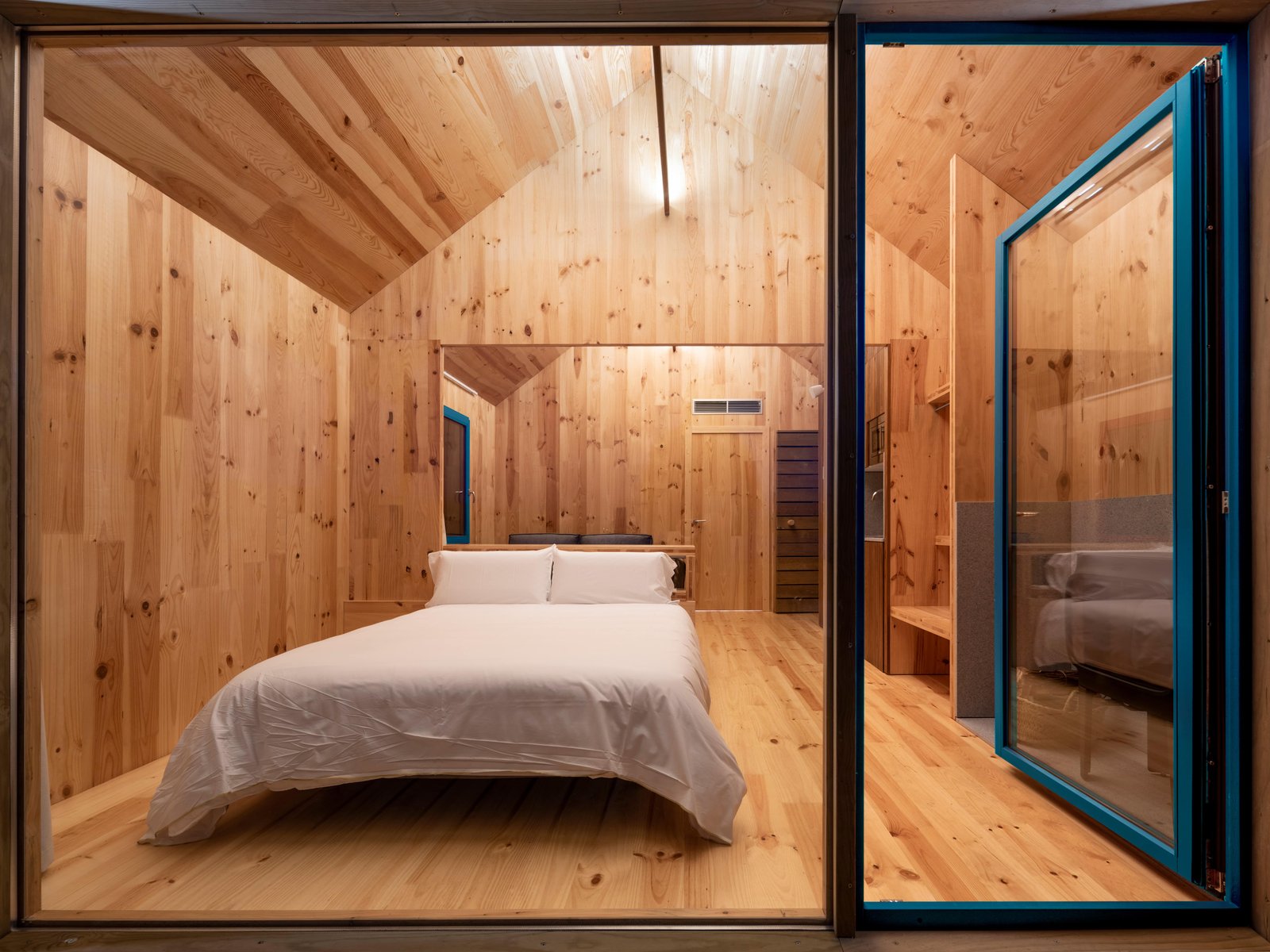 Dormitorio de madera con cama doble y puerta acristalada azul