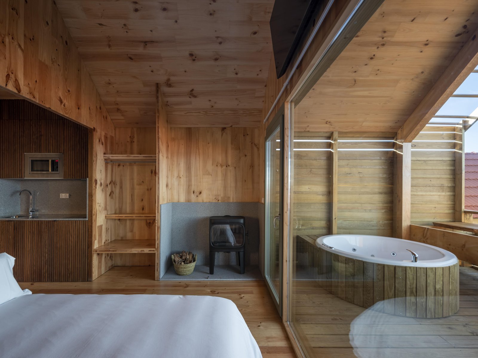 Habitación de madera con bañera de hidromasaje junto a ventanal y cocina integrada