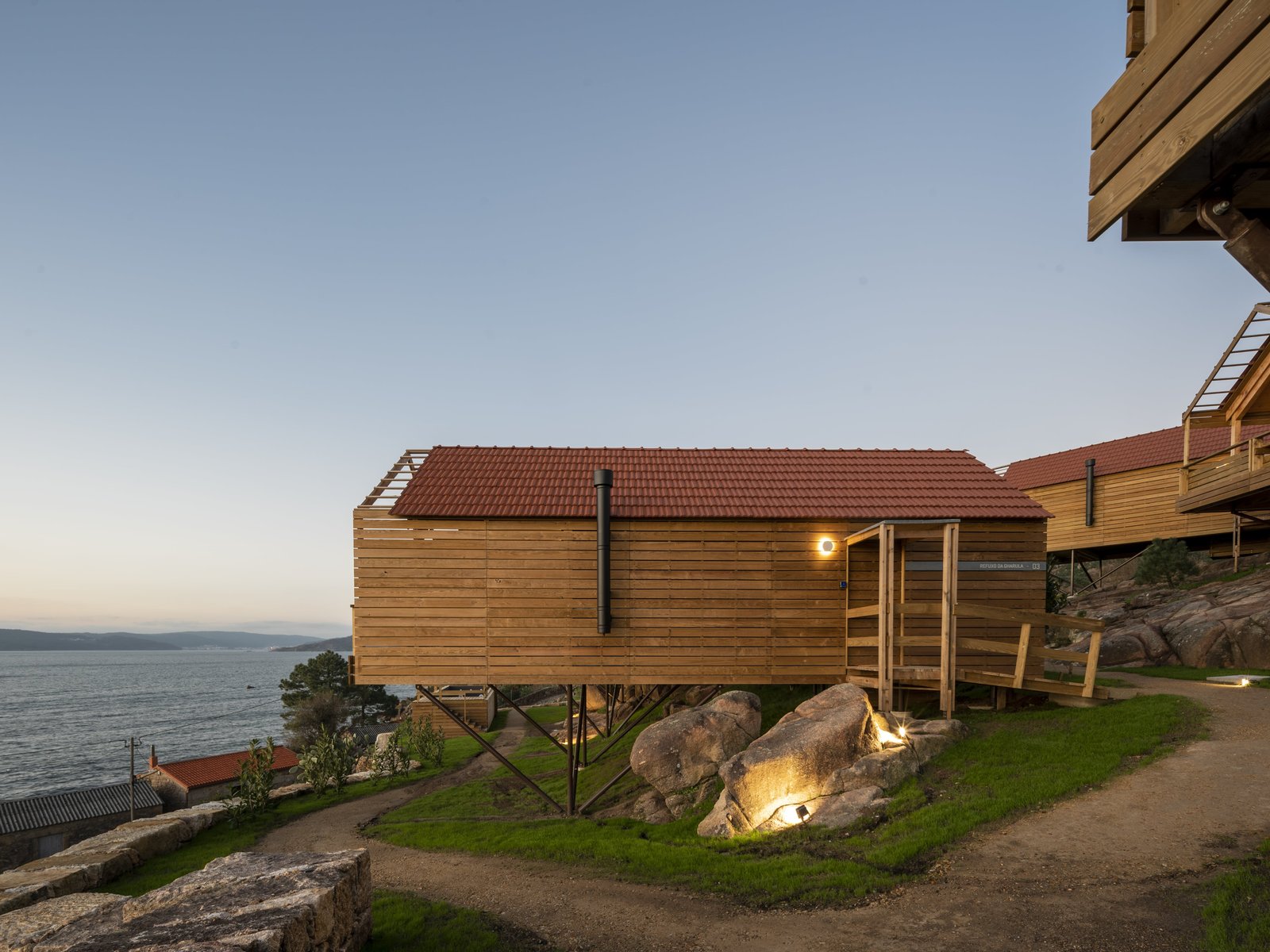 Cabaña de madera elevada sobre rocas junto al mar al atardecer