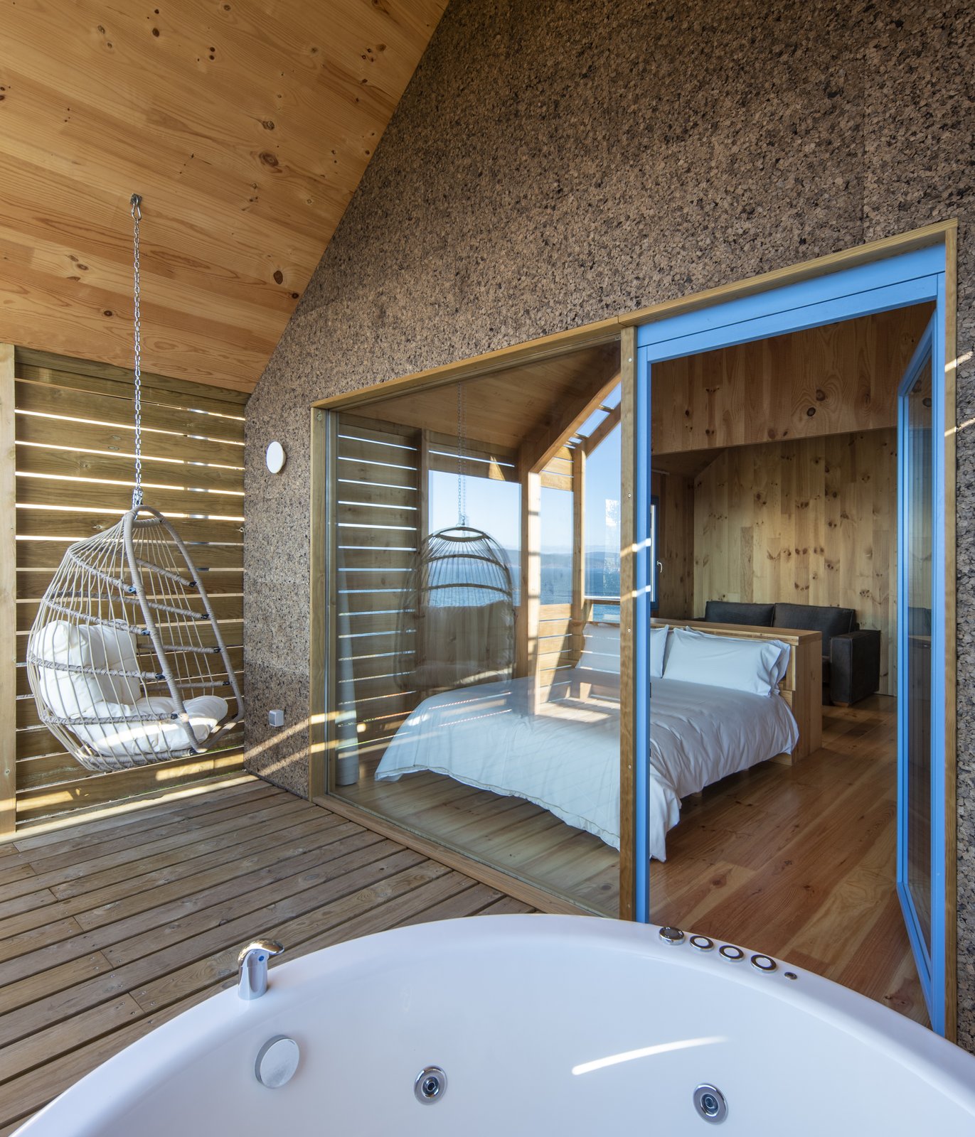 Terraza de madera con bañera exterior y silla colgante frente al dormitorio