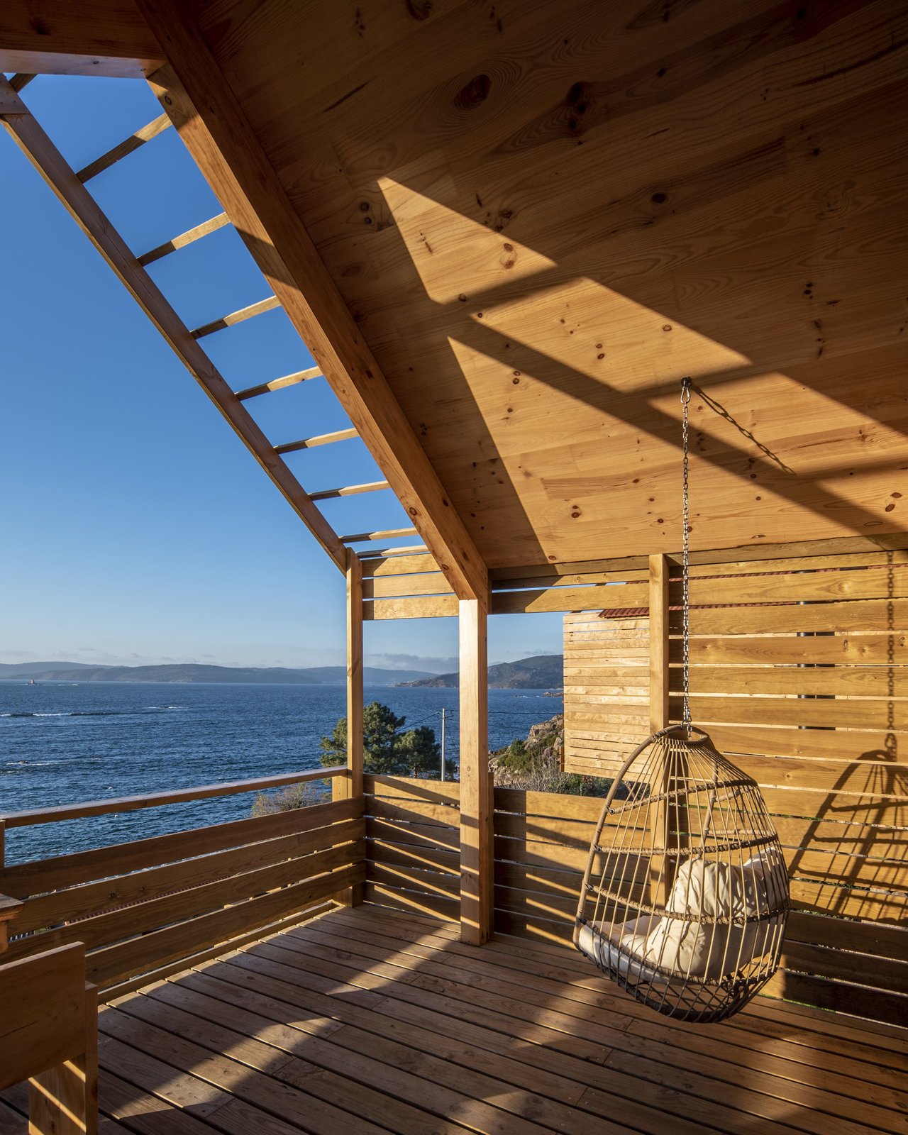 Terraza de madera con sillas colgantes y vista al mar